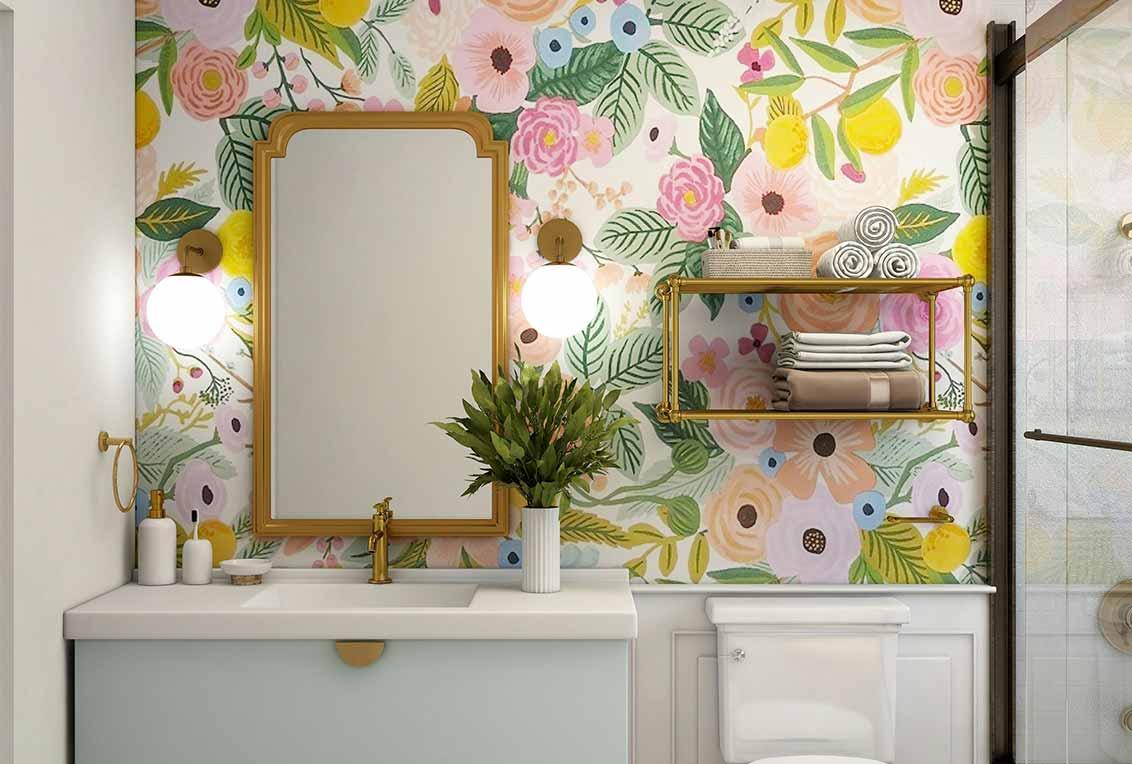 Banheiro com parede estampada com flores coloridas. Na bancada estão dispostos um kit banheiro e uma planta.