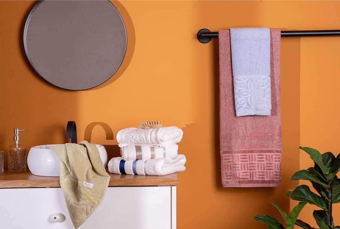 Banheiro com parede laranja com pia e toalhas felpudas
