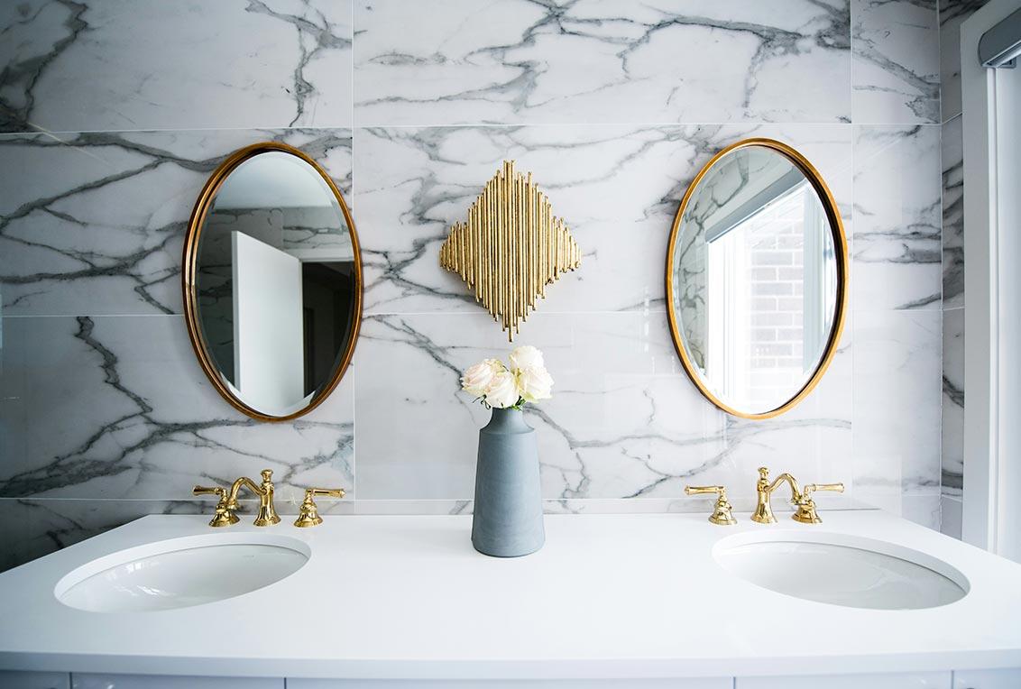 Banheiro com revestimento de azulejo, com espelhos e um buquê de flores na bancada do lavabo. 