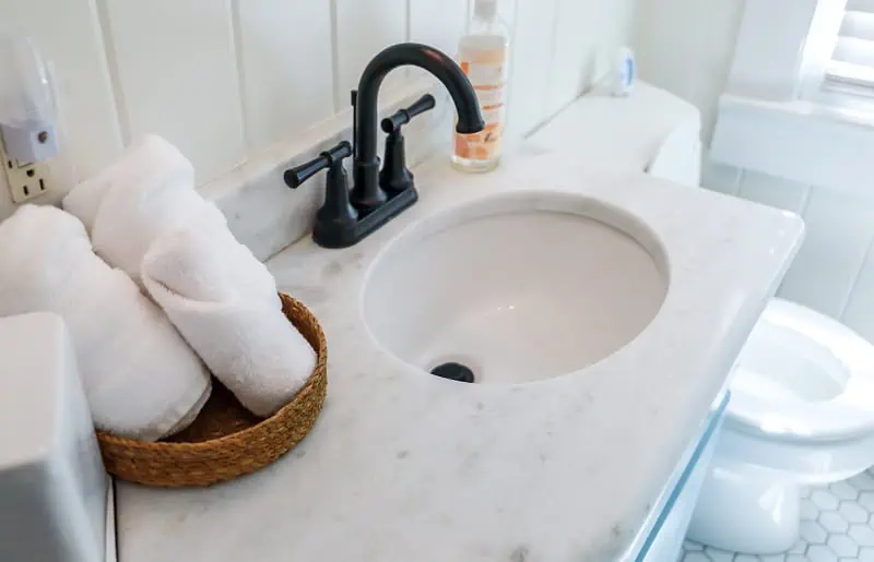 Banheiro simples com pia, toalhas e sabão dispostos na bancada.