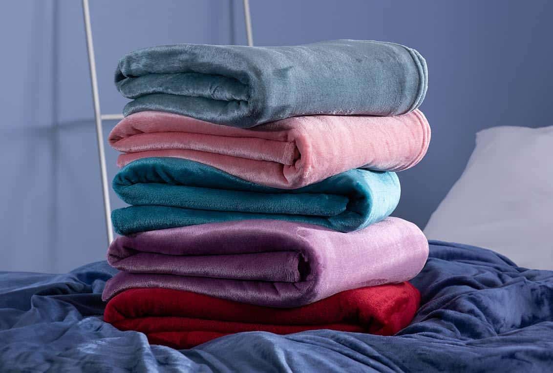 Cobertores de microfibra dobrados, nas cores vermelho, lilás, azul, rosa e cinza